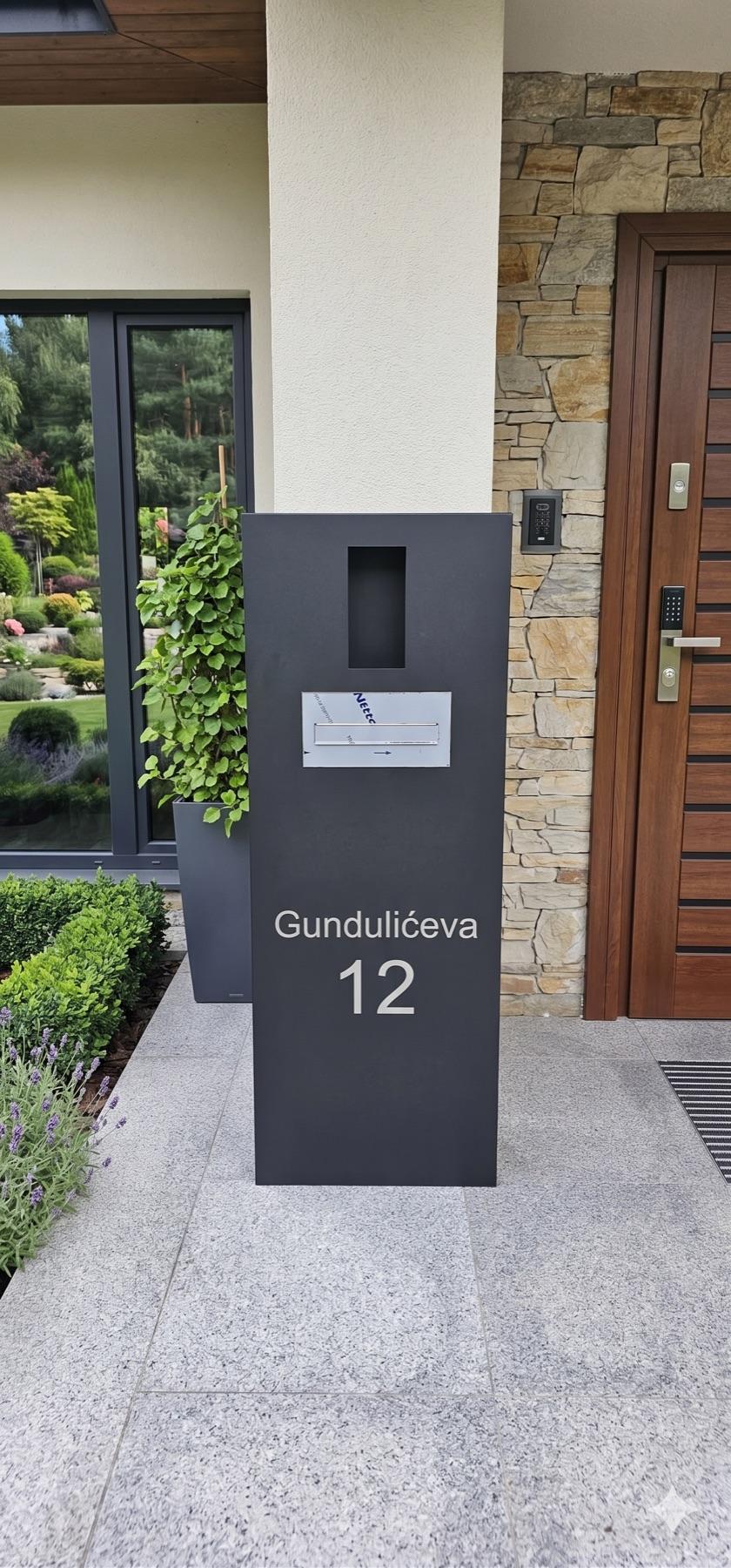 Antracitni multimedijski stup s graviranim kućnim brojem ispred ulaza